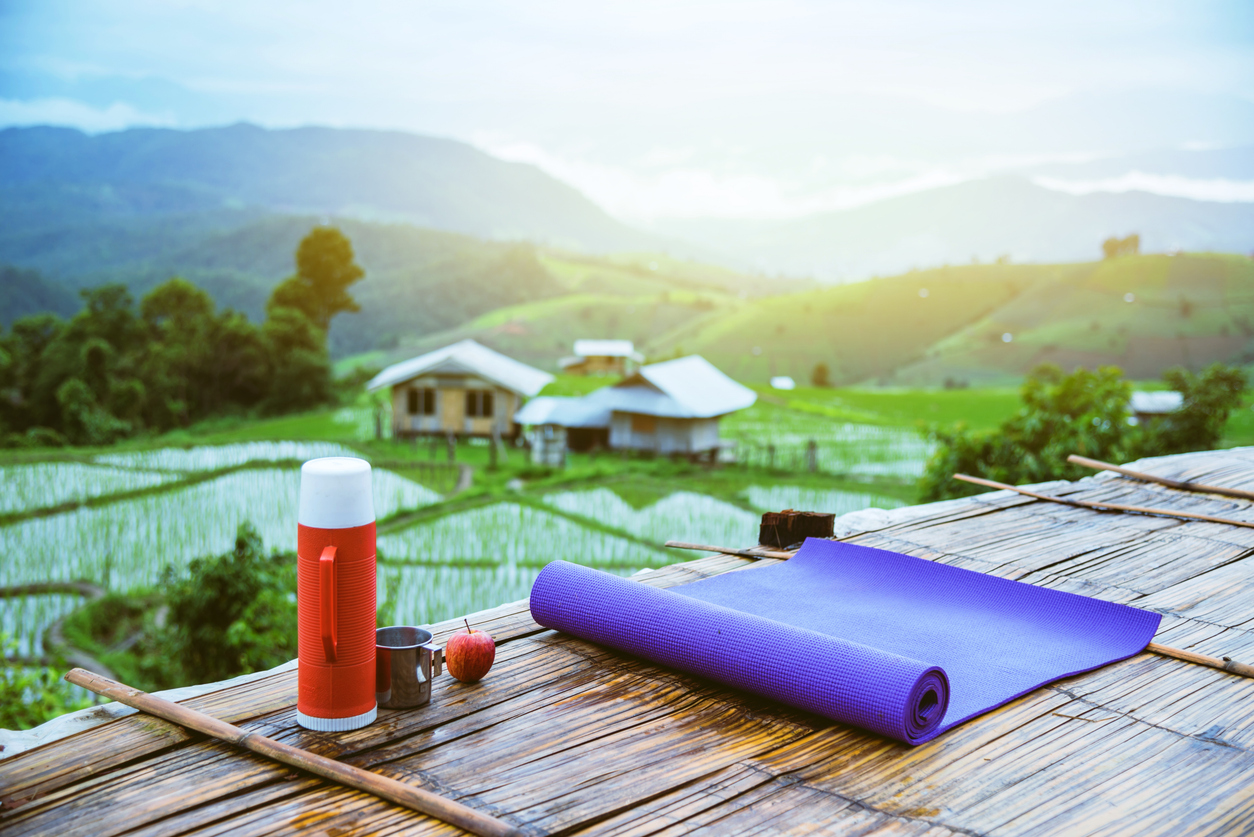Purple yoga mat and red water bottle with a glass of water stainless Put forward. And Red apple on wooden background. On the balcony landscape Natural Field.Travel relax. papongpieng in Thailand