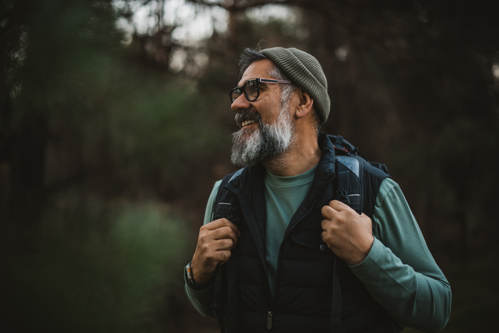 Portrait of mature man with backpack and camera hiking and taking photos in nature.
